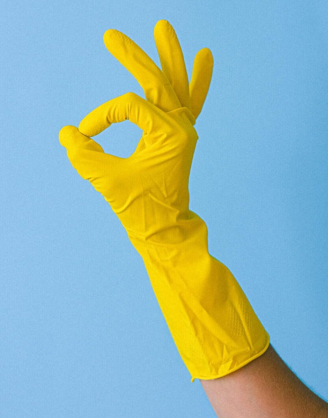 Yellow gloved hand making OK sign against a blue background, symbolizing approval.
